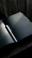 Open notebook with silver pen on dark fabric background, ready for writing, journaling, planning, business notes, education, and creative projects.
