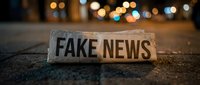 Wooden block with fake news text on urban street at night with blurred city lights creating bokeh effect in background for media literacy concepts.