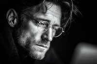Thoughtful middle-aged Caucasian man with glasses and beard in dramatic black and white portrait lighting for professional headshot concepts.