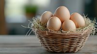 Fresh brown eggs in rustic woven basket with natural hay nest on wooden table, soft focus background creates cozy farmhouse atmosphere.