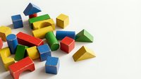 Colorful wooden building blocks in various geometric shapes including cubes, pyramids, and rectangular forms scattered on white surface for educational play and child development.
