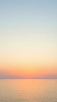 Serene ocean horizon at sunset with soft peachy and coral tones fading into pale blue sky, calm water surface reflecting warm light, tranquil seascape for relaxation and wellness projects.
