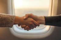 Close-up of business handshake between two people with airplane window in background, symbolizing partnership and travel industry agreements.