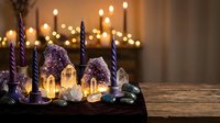 Mystical birthday cake with amethyst crystals, miniature houses and purple candles on wooden table with warm bokeh lights creating magical celebration atmosphere.