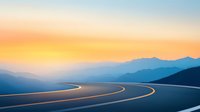 Winding mountain road curves through misty peaks at sunset, dramatic S-shaped asphalt highway leads into distant blue mountains against orange sky.
