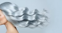 Woman with long, flowing silver-gray hair in waves against neutral background. Side profile portrait showcasing glossy, voluminous hair texture. Suitable for beauty, haircare, and cosmetics marketing.