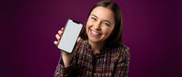 Happy young woman showing blank smartphone screen on purple background for mobile app presentation and digital marketing campaigns.