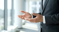 Professional businessman in dark suit holding protective cupped hands gesture in modern office environment for business security and care concepts.
