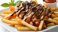 Golden french fries topped with melted cheese sauce and dark chocolate drizzle on white plate, garnished with fresh herbs and orange citrus wedges, served with dipping sauce.