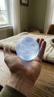 Hand holding glowing crystal ball with swirling blue energy patterns in cozy bedroom setting for fortune telling and mystical practices.