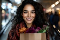 Young mixed race woman with curly dark hair and bright smile holding paper bag with fresh colorful flowers while shopping at local market. Lifestyle portrait.