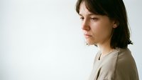 Young Caucasian woman with short dark hair looking down with sad, thoughtful expression, side profile, neutral background, copy space.