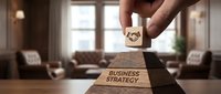 Young adult male hand placing wooden block with gear symbol on top of pyramid stack labeled business strategy in modern office interior setting for corporate planning and growth concepts.