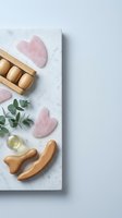 Rose quartz gua sha stones and wooden massage tools arranged on marble surface with eucalyptus leaves and oil for skincare routine.