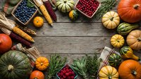 Autumn harvest frame with pumpkins, corn, cranberries and seasonal produce on rustic wooden background. Fall thanksgiving decoration with copy space for text.