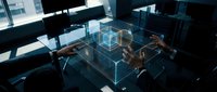 Architects and engineers collaborate around digital holographic building model in modern office workspace with natural light from windows.