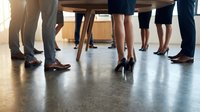 Group of diverse business professionals standing in circle for team meeting or corporate discussion in modern office environment with polished floor.