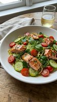 Grilled salmon salad with fresh vegetables and herbs served in white bowl with wine glass on wooden table near window for healthy dining concept.