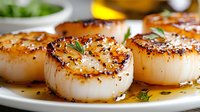 Pan-seared scallops with golden caramelized surface and fresh herbs on white plate. Gourmet seafood dish perfect for fine dining restaurant menus and culinary presentations.