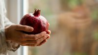 Ripe pomegranate held in hands against blurred natural background, suitable for food, nutrition, health, and wellness marketing materials.