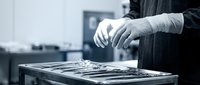 Surgeon in sterile gloves arranging surgical instruments on a metal tray in an operating room, monochrome medical setting.