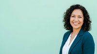 Professional woman with dark curly hair and warm smile wearing navy blazer over white shirt, isolated against soft mint green background for corporate and business use.
