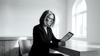 Professional businesswoman with glasses reading tablet in modern office interior with natural window light for corporate presentations.
