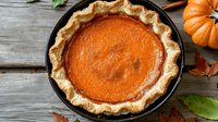 Fresh baked pumpkin pie with flaky golden crust in cast iron skillet on rustic wooden background with autumn decorative elements and fall leaves.