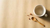 Overhead view of empty ceramic mug with wooden spoon and scattered coffee grounds on neutral beige surface, suitable for beverage, kitchen, and cafe design projects.