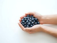 Person holding fresh blueberries in cupped hands against white background. Isolated stock photo suitable for food, health, nutrition, and wellness design projects.
