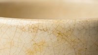 Cracked ceramic bowl surface showing detailed crazing pattern with golden brown lines on cream background for pottery and crafts projects.