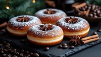 Fresh donuts dusted with powdered sugar, decorated with star anise and cinnamon sticks on dark stone board, coffee beans and Christmas decorations in background.