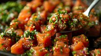 Fresh salmon cubes marinated in Asian-style sauce with green onions and sesame seeds, close up view of glistening raw fish appetizer prepared for poke bowl.
