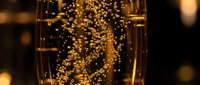 Golden champagne bubbles rising in elegant glass with warm bokeh lights creating luxurious celebration atmosphere for New Year party events.