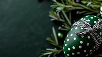 Green Christmas ornament with white polka dots and twine bow beside pine branches on dark background for holiday decorations and seasonal greeting cards.