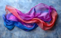 Flowing silk fabric in vibrant pink, coral and blue colors creating dynamic waves and folds against textured gray background. Artistic fashion photography.