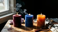 Three colorful burning candles with smoke on wooden surface near window creating cozy atmospheric lighting for relaxation meditation and home decor.