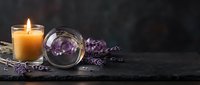 Spa wellness setup with burning candle, amethyst crystals in glass bowl and dried lavender sprigs on dark stone surface for relaxation and meditation.