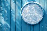 Round snow-covered decorative plate against blue wooden planks background, creating winter seasonal contrast for holiday designs.