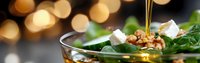 Fresh green salad with mixed greens, walnuts and feta cheese drizzled with golden olive oil against warm bokeh lights background for healthy dining.