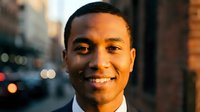 Young African American businessman smiling confidently in urban setting with warm evening lighting and city bokeh background for corporate marketing.