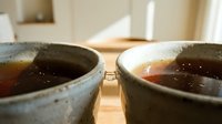 Two ceramic bowls filled with dark tea on wooden surface in warm natural lighting creating cozy atmosphere for relaxation and mindfulness moments.