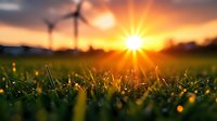 Wind turbines generating clean renewable energy at golden hour sunrise with green grass field and dramatic sky for sustainable power concepts.