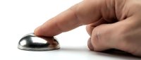 Close-up of human hand touching a metallic dome button or switch against white background for technology and interaction concepts.