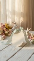 Easter egg shaped gift box with sage green ribbon surrounded by ceramic bunny figurines and dried flowers on rustic wooden table with soft natural lighting.