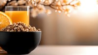 Breakfast cereal in black bowl with fresh orange slice and juice glass, warm morning light and blurred bokeh background for healthy eating and nutrition content.