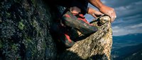 Athletic climber with rope and gear scaling rocky mountain cliff face against dramatic blue sky for outdoor adventure sports.