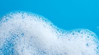 White foam bubbles on bright blue background creating abstract wave pattern for cleaning products and fresh concepts.