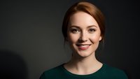 Young professional woman with auburn hair smiling confidently in green sweater against dark background for business and corporate marketing materials.
