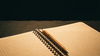 Open spiral notebook with grid pages and metal binding on wooden surface with dramatic lighting.